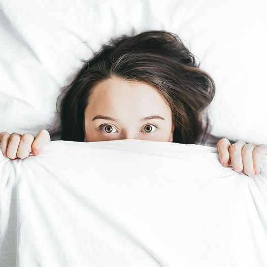 a woman in bed with her face partially covered but her eyes are wide open and she is fully alert