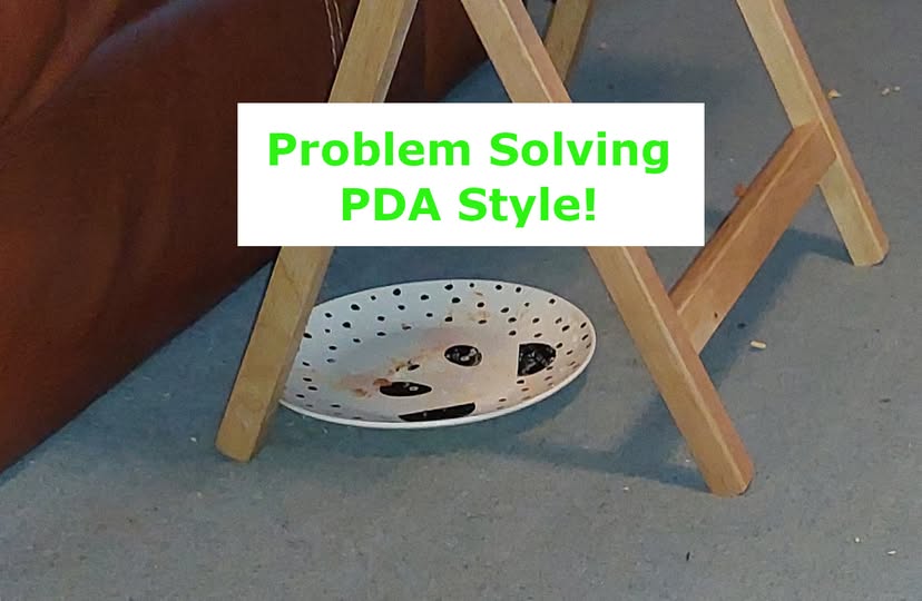 a plate placed on the floor underneath a TV-dinner style table. There are crumbs visible on the floor around the plate.