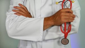 the chest and arms of a man in a white medical coat holding a red stethoscope.